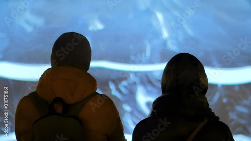 Couple - woman and man admiring modern abstract video on multimedia projection screen on city street at night. Video mapping show, entertainment, sightseeing, digital and contemporary art concept photo