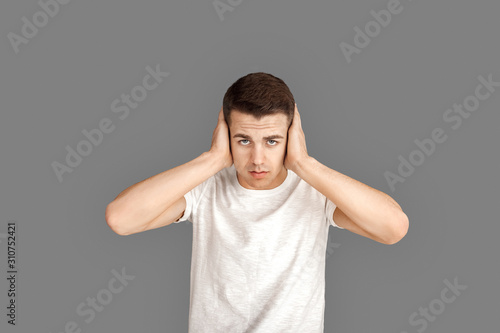 Freestyle. Young man standing isolated on grey covering ears concerned