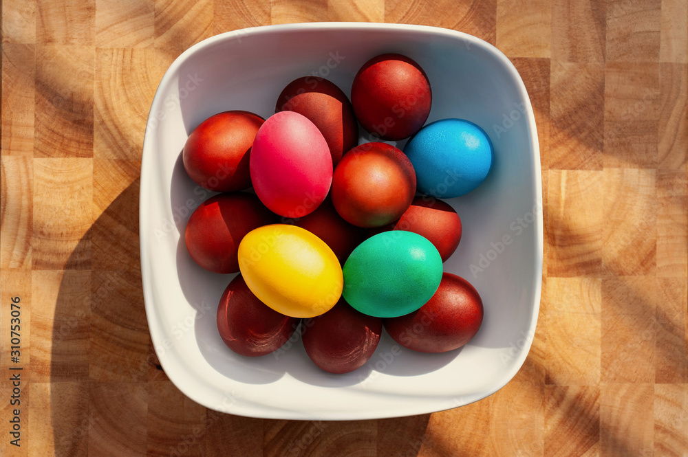 Multicolored Easter eggg in square white bowl on wooden kitchen worktop. Multicolored Easter eggg in square white bowl on wooden kitchen worktop.