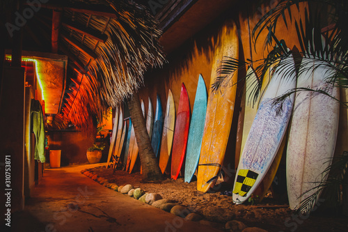 Photography A collection of different colorful surf boards used as a decoration next to a walkway, resting on a wall
