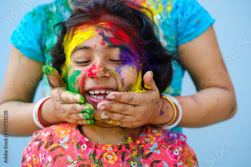 Mother smearing color powder on her daughters face during holi celebration,portrait photo