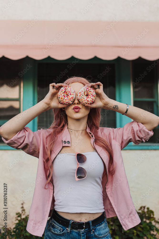 Woman holding donuts over her eyes puckering her lips