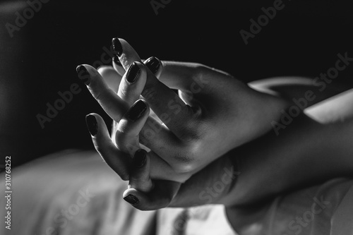 Close up on female young woman's girl's beautiful hands woman lying on the bed black and white nail polish in dark room crossed fingers on sheet gentle passion love temptation emotion concept