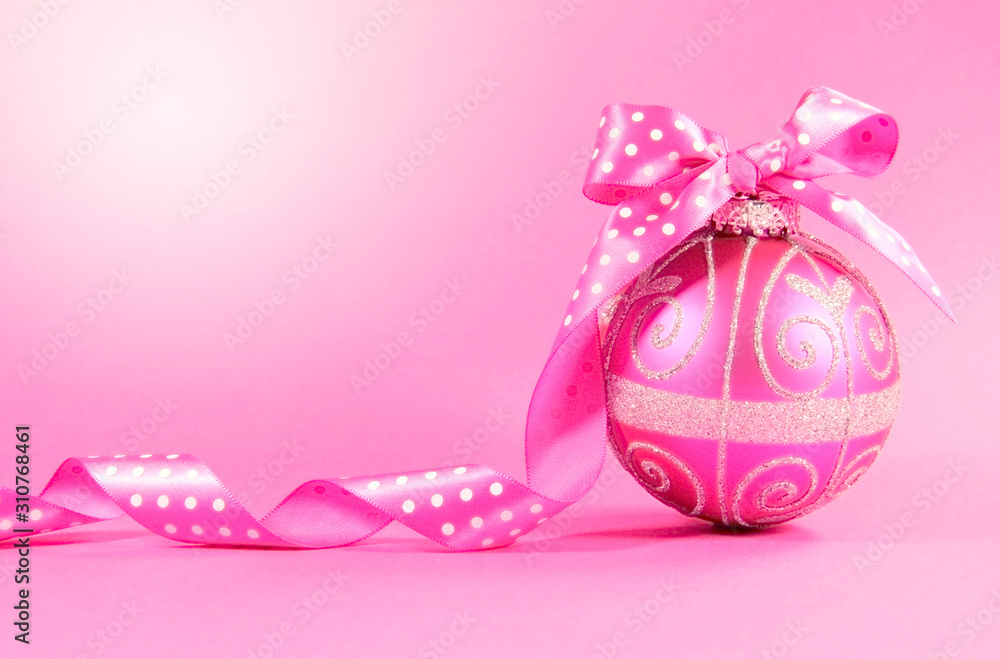 Pink festive bauble ornament with polka dot ribbon on a feminine pink background with copy space for Merry Christmas or Happy Holidays seasons greetings. Lens flare. Pink festive bauble ornament with polka dot ribbon on a feminine pink background with copy space for Merry Christmas or Happy Holidays seasons greetings. Lens flare.