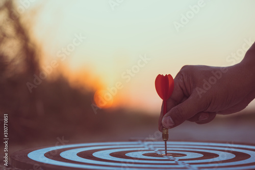 Fotografía Close up hand hitting red arrow to target dartboard at sunset background