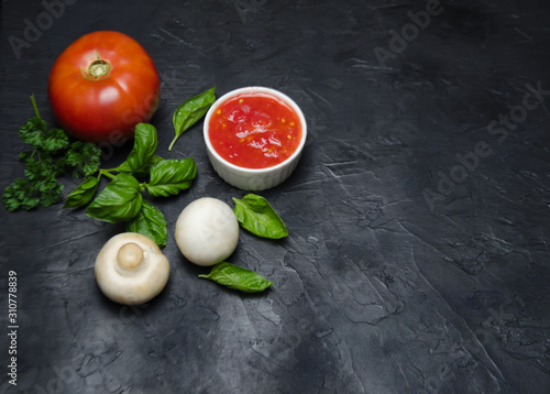 red tomato and mushrooms championsa near greens Basil lie with a Cup of sauce on a black background