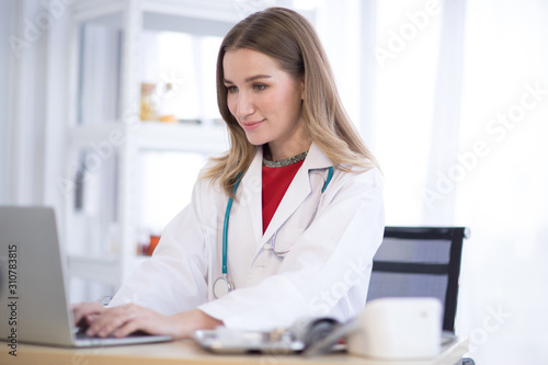 A female doctor wearing a white coat in the hospital is typing a computer