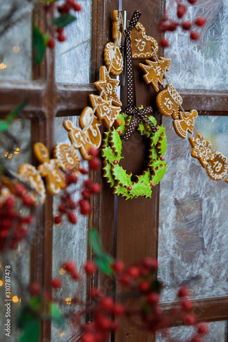 Beautiful Christmas gingerbread wreath and advent calendar hanging on a wooden window. Frosty glass pattern. Winter december day. Xmas mood. Vertical frame