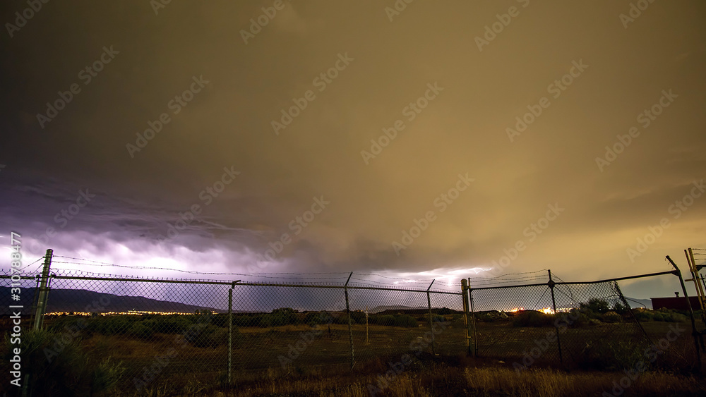 Lightning storm on the horizon looking through chain link fence in Utah.