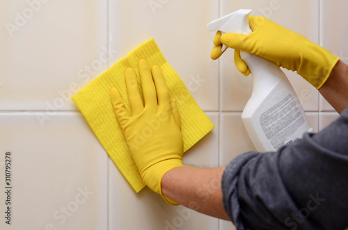 Man in yellow rubber gloves washing tiles with spray cleaner and sponge