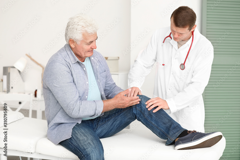 Doctor examining mature man with joint pain in clinic Doctor examining mature man with joint pain in clinic