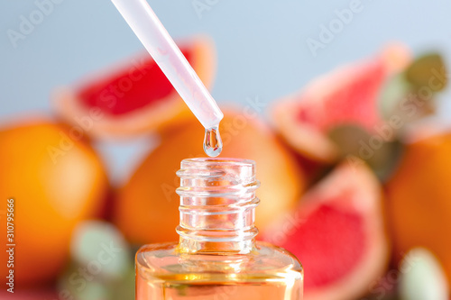 Grapefruit oil dripping into bottle on blurred background, closeup photo