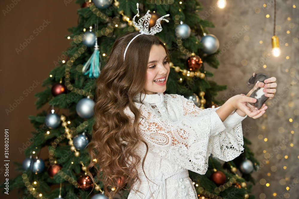 Beautiful girl with wavy hair in a white dress holding a rat. Christmas. The year of the steel rat. Xmas portrait with 2020 new year symbol animal. Beautiful girl with wavy hair in a white dress holding a rat. Christmas. The year of the steel rat. Xmas portrait with 2020 new year symbol animal.