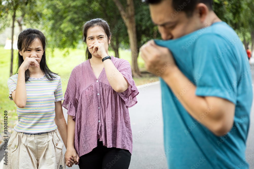 Asian man check his own smell,sniffing his wet armpit or sweating a lot because of hot weather or after exercise,husband bad smell while wife and daughter closing her nose,child girl feel stinks