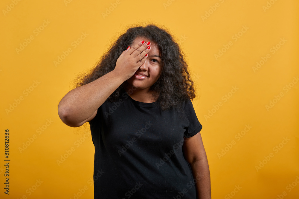 Attractive young afro-american woman with overweight covering eye with hand, smiling over isolated orange background wearing fashion black shirt. People lifestyle concepte. Attractive young afro-american woman with overweight covering eye with hand, smiling over isolated orange background wearing fashion black shirt. People lifestyle concepte.
