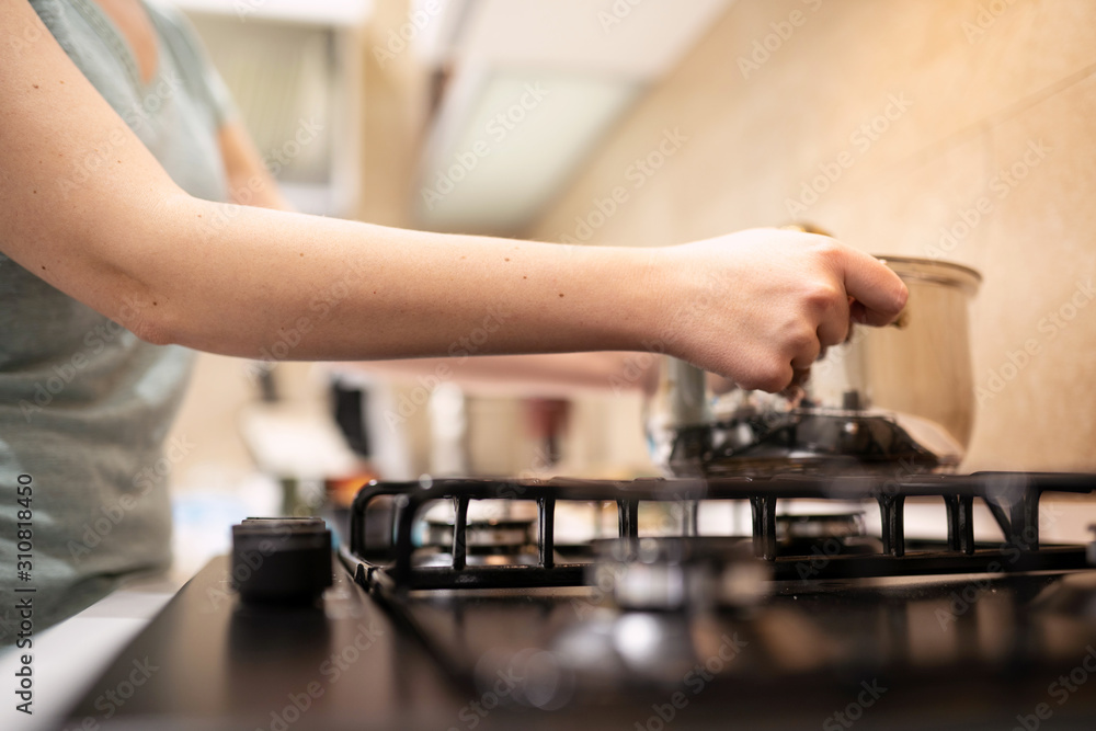 Beautiful young woman housewife prepairing dinner, hold in hands big steel saucepan, standing it on gas-stove. Beautiful young woman housewife prepairing dinner, hold in hands big steel saucepan, standing it on gas-stove.