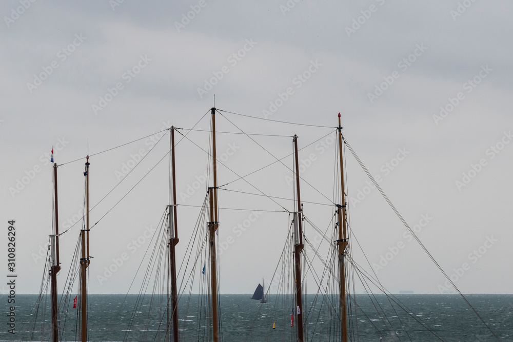 Sailboat at sea seen through the masts of two three-masted sailboats.