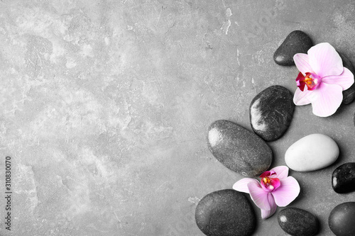 Stones with orchid flowers and space for text on grey background, flat lay. Zen lifestyle