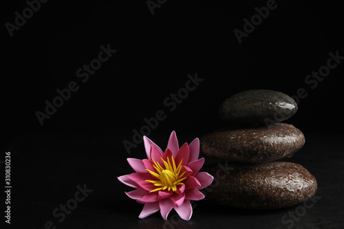 Stones and lotus flower on black background, space for text. Zen lifestyle