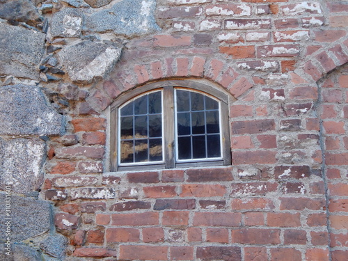Wall of a medieval castle of stone and brick and a window in it © HelenkaNNN