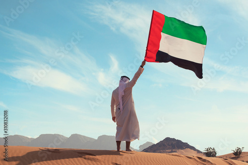Proud arabian Emirati man holding a UAE flag in the desert