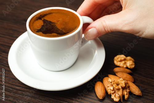 Close-up of young female hand reaching for the cup of coffee. Cup and nut fruits lying on dark wooden table. Loneliness and solitude