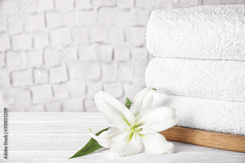 Stack of clean bath towels and beautiful flower on white wooden table. Space for text