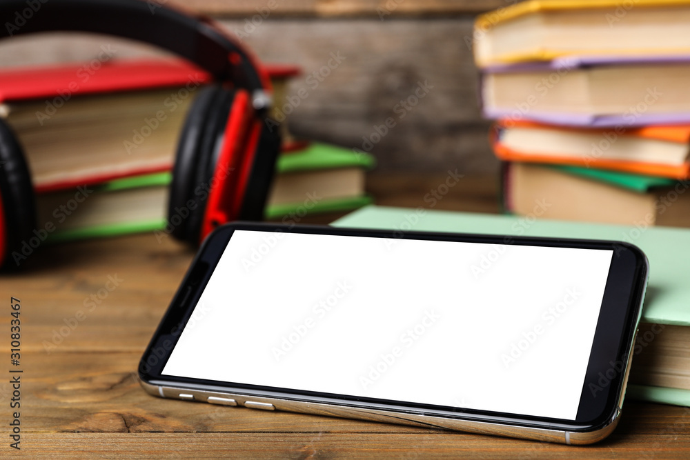 Modern smartphone with blank screen and books on wooden table, closeup. Space for design