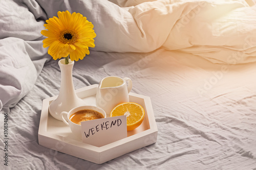 Tray with coffee, milk, orange, yellow flower in a vase and card with text Weekend