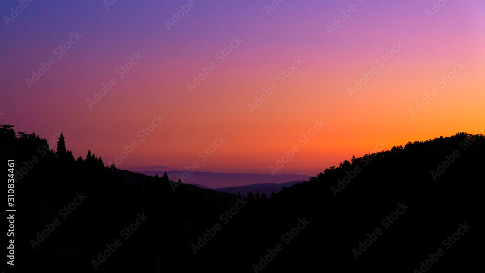 silhouette of trees and hills under orange and  purple sky during sunrise