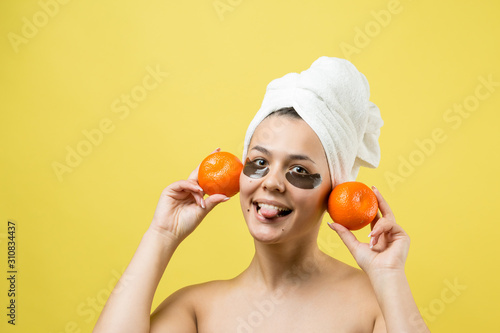 Beauty portrait of woman in white towel on head with gold nourishing mask on face. Skincare cleansing eco organic cosmetic spa relax concept. A girl stands with her back holding an orange mandarin.