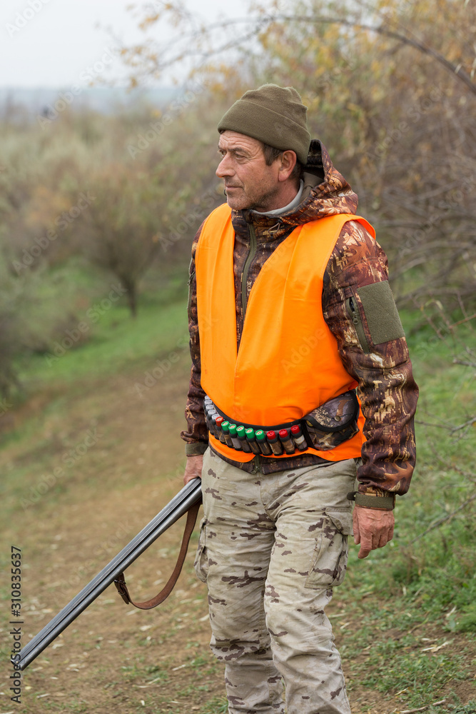 Hunting period, autumn season open. A hunter with a gun in his hands in hunting clothes in the autumn forest in search of a trophy. A man stands with weapons and hunting dogs tracking down the game. Hunting period, autumn season open. A hunter with a gun in his hands in hunting clothes in the autumn forest in search of a trophy. A man stands with weapons and hunting dogs tracking down the game.
