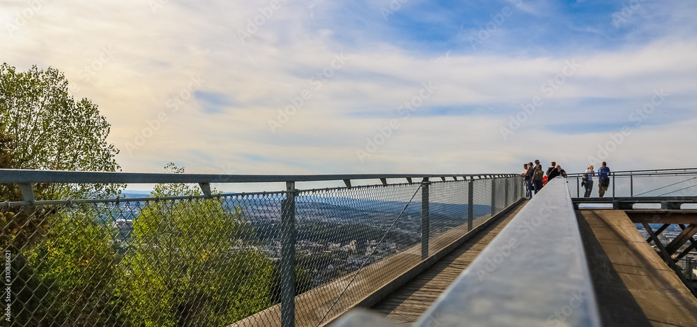 Fototapeta premium Panoramic view along the handrail of the wooden Rhine viewing platform at the peak of the hill next to the Ehrenbreitstein Fortress in Koblenz, Germany on a nice autumn day with a blue sky.