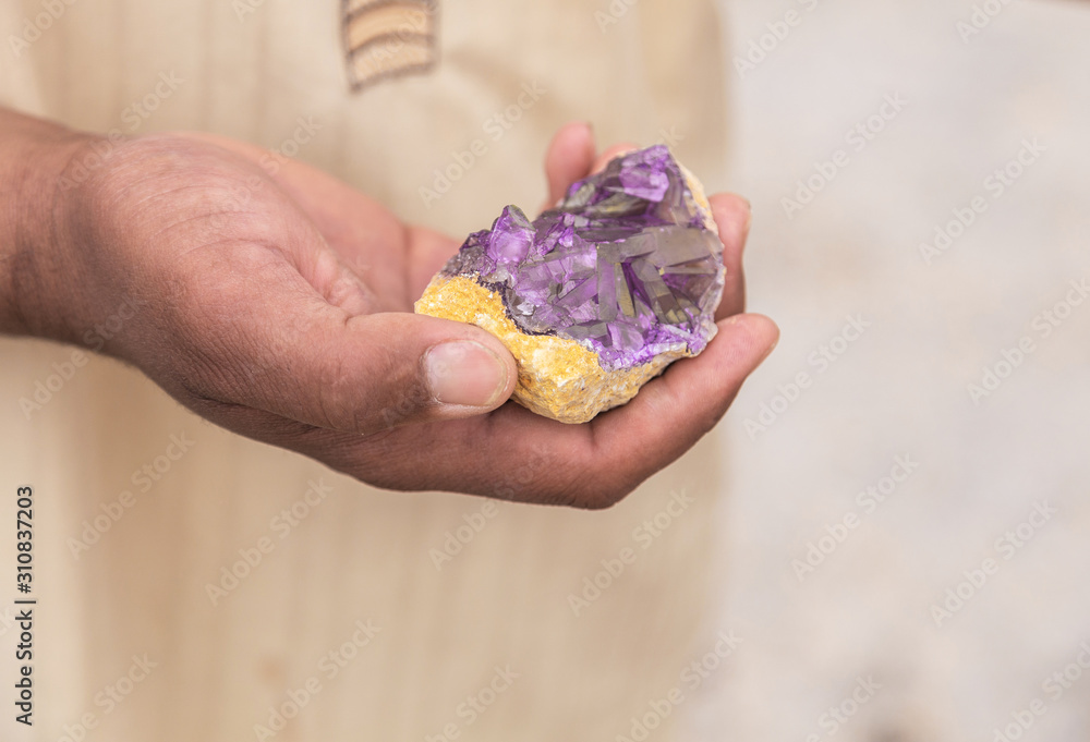 Closeup view of male hand holding beautiful colourful stone. Arabian man proposing tourists to buy stone as souvenir. Tounisia country. Horizontal color photography.