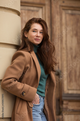 Young woman standing near a wood door. Portrait. Vertical.