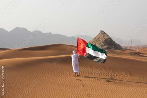 Arab man holding the UAE flag in the desert celebrating UAE national day and Uae flag day.