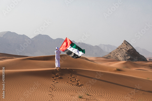 Arab man holding the UAE flag in the desert celebrating UAE national day and Uae flag day.