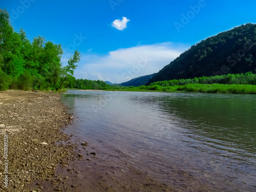 Landscape of the Tisza river on the background of the Carpathians near Khust (Transcarpathia, Ukraine). Beautiful natural panorama: water, mountains and a stone beach on a sunny spring day