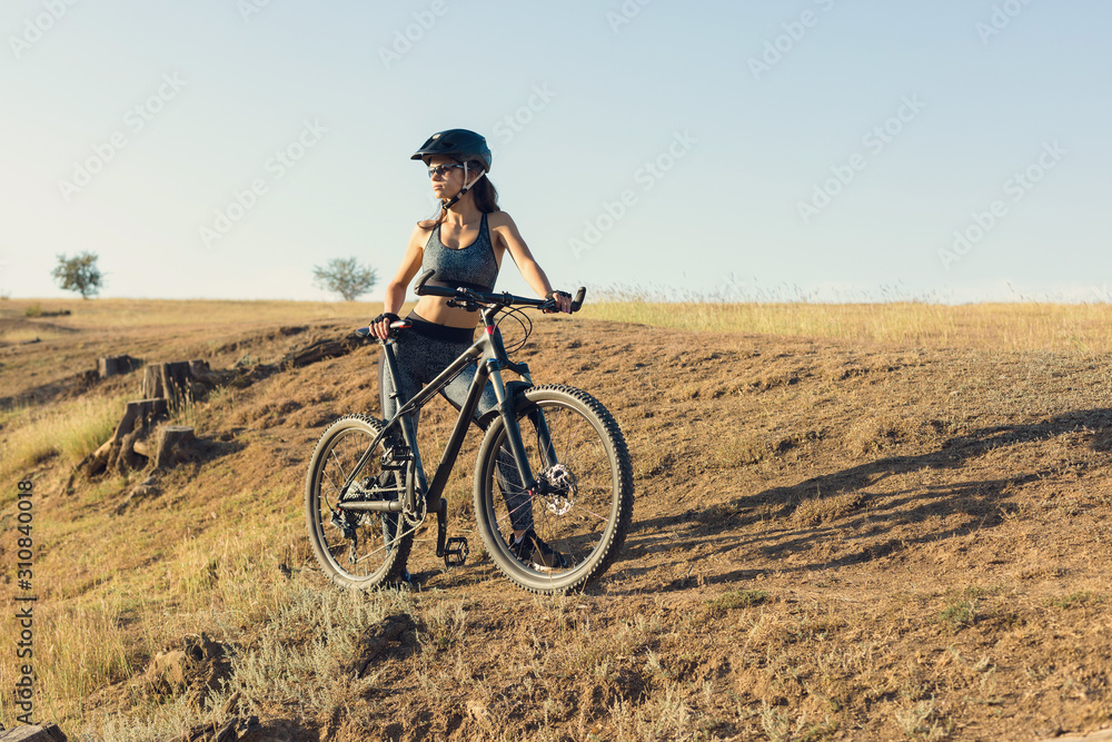 Girl on a mountain bike on offroad, beautiful portrait of a cyclist at sunset, Fitness girl rides a modern carbon fiber mountain bike in sportswear. Close-up portrait of a girl in a helmet and glasses Girl on a mountain bike on offroad, beautiful portrait of a cyclist at sunset, Fitness girl rides a modern carbon fiber mountain bike in sportswear. Close-up portrait of a girl in a helmet and glasses