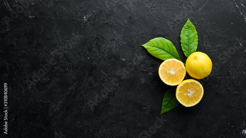 Fresh yellow lemons with leaves. Citrus fruits on black stone background. Top view. Free copy space.