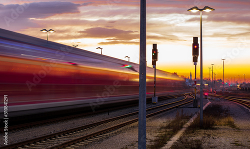 A commuter train leaves a station shortly after sunset