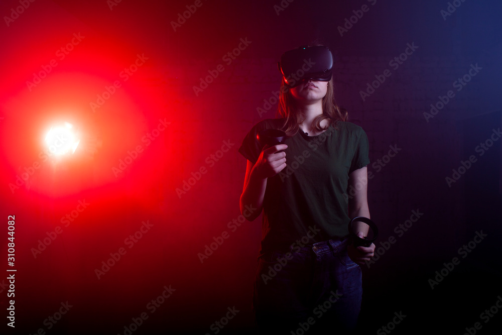 girl gamer stands in a virtual reality game room and holds VR devices, a woman plays a shooter at night girl gamer stands in a virtual reality game room and holds VR devices, a woman plays a shooter at night
