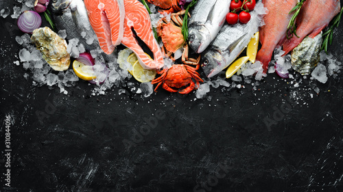 Seafood: Dorado, salmon, crab, grouper, oysters. On a black stone background. Top view. Free space for your text.