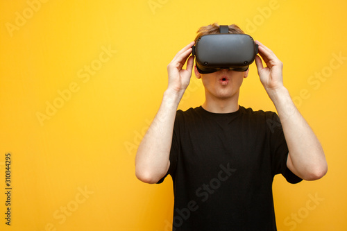 surprised young guy with VR glasses on a yellow background looks at the horror and screams, man use virtual reality glasses and be afraid