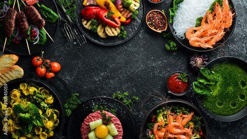Assorted food and dishes of vegetables, meat and fish on a black stone background. Top view. Free space for your text.