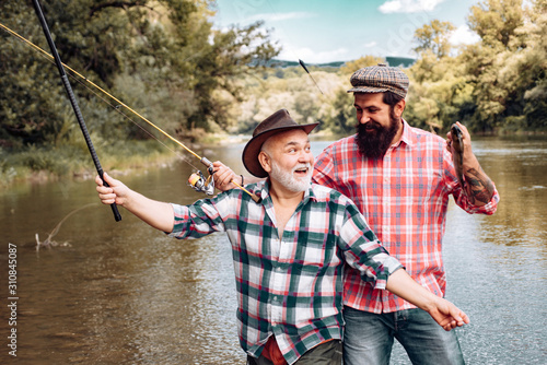 Portrait of cheerful two bearded men fishing. Fishermen fishing equipment. Fly fishing. Fish normally caught in wild. Happy fishermen. Summer weekends or vacation. Real happiness.