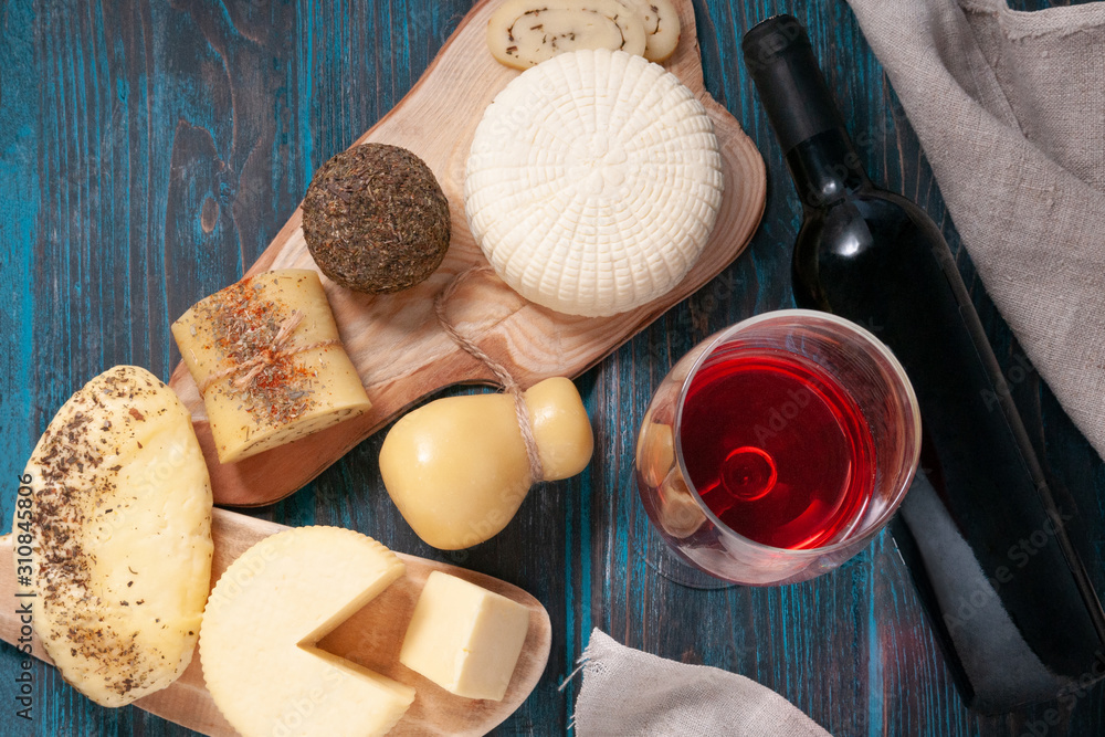 A set of cheeses. Halumi, Caciotta, Caciocavallo, cheese sticks, Suluguni, Belper knolle, cheese roll with Provencal herbs..On wooden boards. Next to the cheese bottle and a glass of red wine. A set of cheeses. Halumi, Caciotta, Caciocavallo, cheese sticks, Suluguni, Belper knolle, cheese roll with Provencal herbs..On wooden boards. Next to the cheese bottle and a glass of red wine.