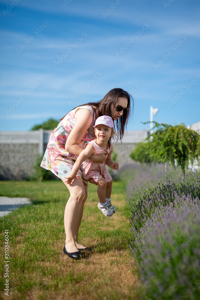 Obraz premium Happy mother and daughter in the park. Beauty nature scene with family outdoor lifestyle. Happy family resting together on the green grass, having fun outdoor. Happiness and harmony in family life