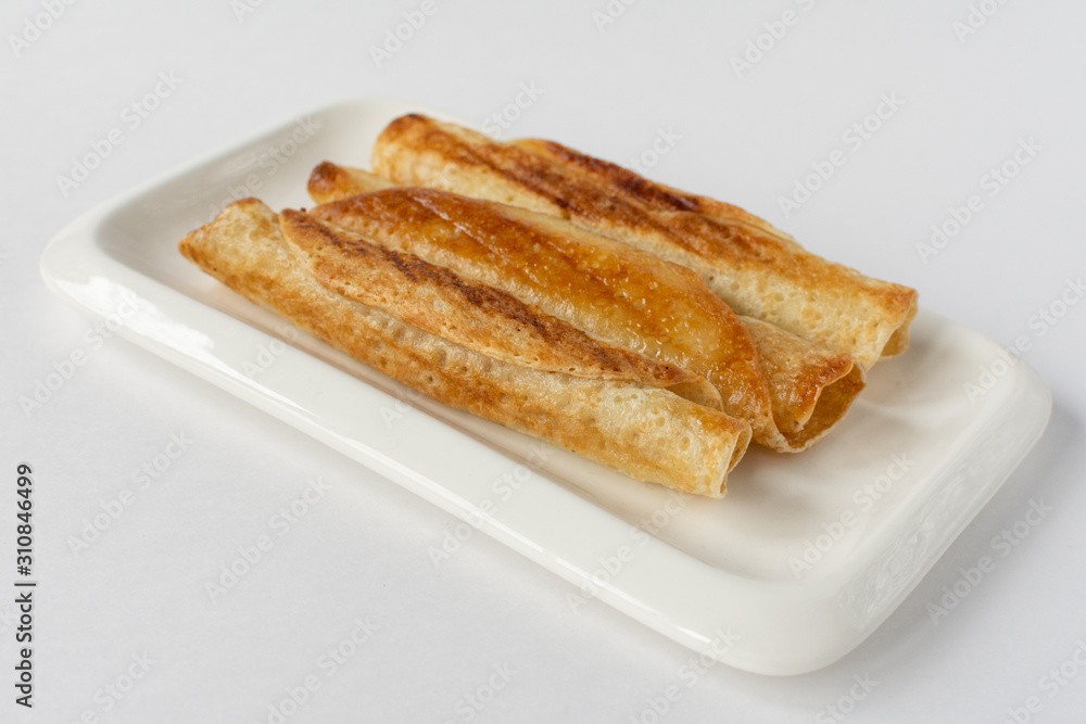 Fried pancakes roll into a tube on a white plate with a white background.