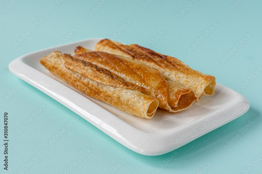 Fried pancakes roll into a tube on a white plate with a blue background. Fried pancakes roll into a tube on a white plate with a blue background.